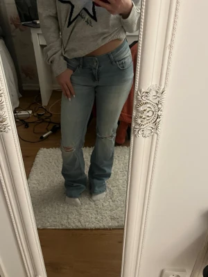 Bootcut ljusblå jeans med slitningar - Säljer ett par ljusblå bootcut jeans med snygga slitningar vid knäna. Jeansen har låg midja och är bootcut! Aldrig använda! De är däremot felmärkta så det står att det är storlek 46 i dom men den verkligen storleken skulle jag uppskatta till 34!