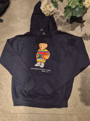 Marinblå polo bear ralph lauren - * 🧥 Typ: Pullover-hoodie (utan dragkedja) * ✨ Skick: Nyskick – mycket fint skick utan synligt slitage * 🎨 Färg: Mörk svart/mörkgrå, jämn och fräsch ton * 🏷️ Märke: Nike – stilren vit logotyp på vänster bröst * 🧵 Material: Mjuk och följsam bomullsblandning av hög kvalitet * 👕 Passform: Bekväm och klassisk, lätt oversized känsla * 🧢 Huva: Huva med justerbara dragsnören * 🧤 Detaljer: Praktisk magficka framtill * 👌 Stil: Tidlös och lättmatchad för både vardag och träning