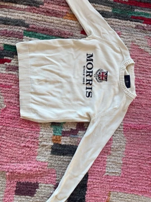 Vit stickad tröja från Morris - Snygg stickad tröja från Morris med broderad logga och brittisk flagga på bröstet. Tröjan har rund halsringning, ribbade muddar och lång ärm. Perfekt för en stilren och klassisk look. Pris kan diskuteras!