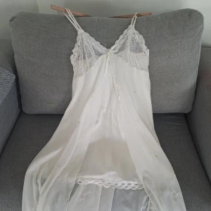 Vit långnattlinne med spets och rosett - Romantisk vit nattlinne med tunna axelband, vacker spets upptill och liten rosett framtill. Perfekt för dig som gillar en feminin och drömmig stil. Köpt i Dubai och i fint skick 