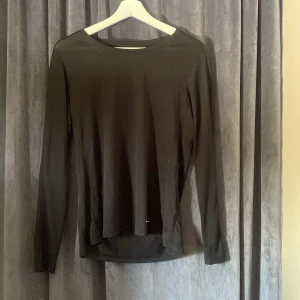 Svart långärmad träningströja Ronhill - Svart långärmad träningströja från Ronhill i storlek M. Tillverkad i 100% polyester, perfekt för löpning eller gym. Enkel och stilren design med rund hals och smal passform som sitter skönt mot kroppen.