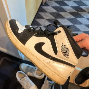 Nike Air Jordan 1 svart/vit EUR 42 - Säljer ett par Nike Air Jordan 1 i svart och vitt skinn med klassisk Jordan-logga på sidan. Skorna har svarta snören, perforerad tå och hög siluett. Perfekta för dig som gillar streetstyle och vill sticka ut med en ikonisk sneaker. Finns bara skor.