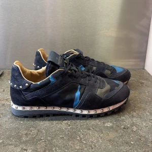 Valentino Rockrunner sneakers blå camouflage - Snygga Valentino Rockrunner sneakers med blå och gröna camouflagepaneler i mocka och textil. En del av nitraden på vänster bak sitter relativt löst (bild 4), men det går att laga enkelt med lite lim. Orginalboxen medfås.