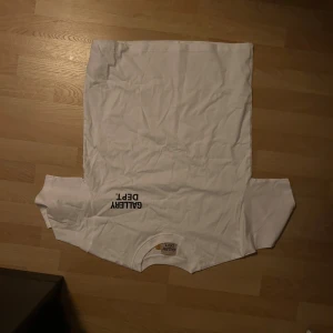 Vit t-shirt från Gallery Dept. S - Vit t-shirt från Gallery Dept. med svart tryck på bröstet och ryggen där det står 'GALLERY DEPT. HOLLYWOOD, CA.'. Klassisk rund hals och korta ärmar. Tillverkad i mjuk bomull för en clean och enkel look. Aldrig använd jätte bra skick de står att den är s i storlek men den känns större så den skulle nog passa en medium också.