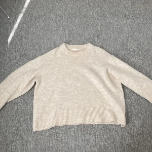 Beige stickad tröja från Gina Tricot - Mysig beige stickad tröja från Gina Tricot med rund halsringning och bred ribbad kant nedtill. Tröjan har en loose passform och långa ärmar. Den är knappt använd