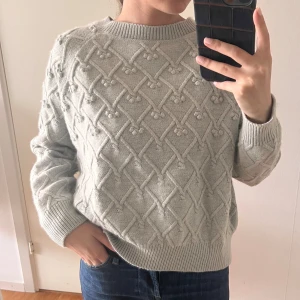 Ljusgrå stickad tröja med strukturmönster - Superfin ljusgrå/grön (skiftar i olika ljus) stickad tröja med unikt strukturmönster i form av korsade linjer och små bollar. Tröjan har rund halsringning, ribbade muddar och lång ärm. Perfekt för dig som gillar mysiga och snygga plagg med det lilla extra. Lappen är borttagen i nacken. 