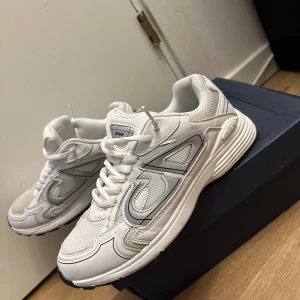 Vita dior b30 - Säljer ett par vita Dior sneakers med reflekterande CD-detaljer på sidorna. Skorna har en chunky sula, snörning och är tillverkade i en mix av mesh och skinn. Perfekta för dig som vill sticka ut med en clean och modern look.