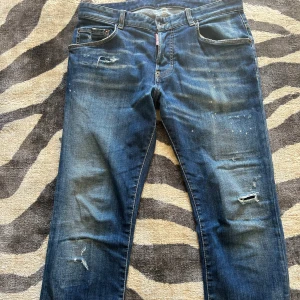 Blå Dsquared2 jeans med slitningar - Snygga blå jeans från Dsquared2 med coola slitningar och distressed detaljer både fram och bak. Klassisk femficksmodell med raka ben och normal passform. Tillverkade i bomull med stretch för extra komfort. Perfekta för dig som gillar en avslappnad och trendig look.