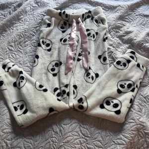 Panda mjukisbyxor från Censored - Supergosiga vita mjukisbyxor från Censored med sött pandamönster och breda rosa satinsnören i midjan. Byxorna är fluffiga och perfekta för chill hemma. De har resår i midjan och är tillverkade i mjuk fleece för extra mysfaktor.storlek xxs passar för 9-11 år