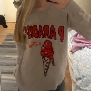  Intressekoll på min from future tröja  - Säljer en beige stickad tröja med tryck i rött och orange som säger 'PARADISE' och har en glass i strut på framsidan. Tröjan har lång ärm och en avslappnad passform, perfekt för dig som gillar coola prints och vill sticka ut lite extra. 