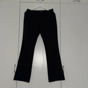 Svarta kostymbyxor med slits - Snygga svarta kostymbyxor med bootcut och slits nertill på benen. Byxorna har bälteshällor och fickor bak, vilket ger en clean och stilren look. Perfekta för dig som gillar klassiska men trendiga vibes.