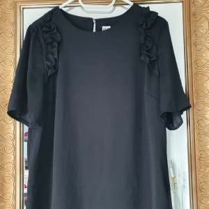 Svart blus Saint Tropez S - Svart blus från Saint Tropez i storlek S. Klänningen har rund hals, korta ärmar och snygga volangdetaljer längs axlarna. I gott skick 