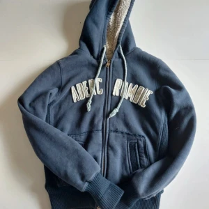 Fodrad abercrombie hoodie  - Mysig mörkblå hoodie från Abercrombie med dragkedja, broderad logga framtill och fodrad huva i teddy. Tröjan har snörning i huvan, ribbade muddar och två fickor framtill. Passar storlek M-XS. På lappen så stor der storlek L, men den passar mig som har storlek XS. Har även tvättat hoodien efter dessa bilder togs, då eventuellt smuts är nu borta. 