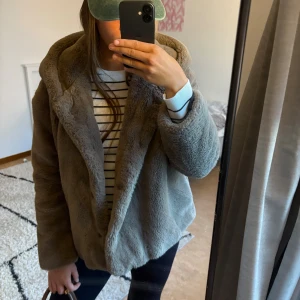 Beige pälsjacka med huva - Säljer en fluffig och mysig beige pälsjacka med stor huva. Jackan har en loose passform och är perfekt för kalla dagar. Materialet är mjukt och ger en chill vibe, passar dig som gillar att sticka ut med en cozy look. Flera skador inuti jackan dock med trasiga fickor och trasiga armar men utanpå är den helt utan defekter 