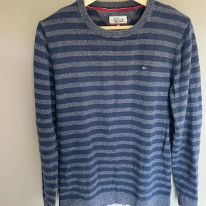 Randig blå tröja Tommy Hilfiger - Snygg blåmelerad tröja från Tommy Hilfiger Denim med gråa horisontella ränder. Klassisk rund halsringning och diskret logga på bröstet. Långärmad och i mjukt material, perfekt för en chill och stilren look.