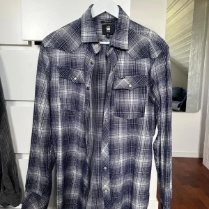 Rutig blå skjorta från G-Star RAW - Slim fit skjorta från G-Star RAW i blått och vitt rutigt mönster. Skjortan har långa ärmar, två bröstfickor med knappar och klassisk krage. Perfekt för dig som gillar en clean och modern stil. Nypris 800