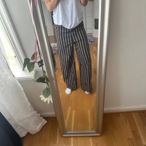 Svarta vida randiga byxor - Säljer ett par svarta byxor med vita vertikala ränder och bred passform. Byxorna har hög midja och raka, vida ben som ger en chill och trendig look. Perfekta för dig som gillar bekväma och snygga byxor med lite edge.