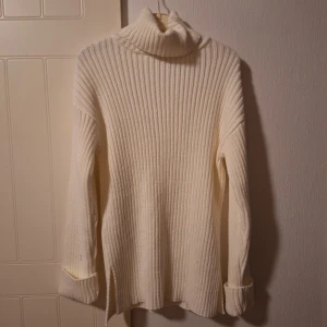 Vit ribbad polotröja från NA-KD - Säljer en vit polotröja från NA-KD i storlek S. Tröjan är ribbstickad med lång ärm och hög polokrage, perfekt för lager-på-lager. Materialet är mjukt och stickat, med snygga slitsar i sidorna och breda muddar vid ärmsluten. Den ät lång i kroppen men skulle nog kunna stylas snyggt med ett par jeans eller kostymbyxor🥰