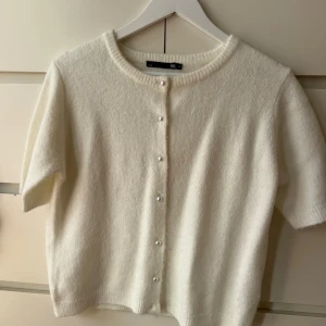 Vit kofta med pärlknappar  - Superfin vit kofta från Lager 157 med korta ärmar och rund hals. Koftan är stickad och har snygga pärlknappar framtill som ger en söt touch. 