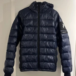 Mörkblå pufferjacka från Peak Performance - Snygg vinter jacka från PeakPerformance. Använts varsamt. Perfekt för kyliga dagar.