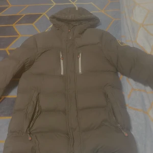 Svart pufferjacka Zavetti Canada S - Svart pufferjacka från Zavetti Canada med huva, stora dragkedjefickor och reflekterande rand på huvan. Jackan är quiltad och har innerfoder i fleece för extra värme. Perfekt för kalla dagar och snygg streetstil. Helt ny, oanvänd.