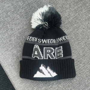 Svart Åre mössa med tofs och brodyr - Säljer min fantastiska Åre mössa i svart färg. Köpt förra vintern i Åre och bara använd då (2 veckor). Både tjej och kille kan använda den. Pris kan diskuteras?