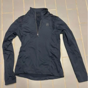 Mörkblå långärmad tröja från Hööks - Sportig mörkblå långärmad tröja från Hööks med halv dragkedja framtill och diskreta meshdetaljer på axlarna. Perfekt för ridning eller träning, med en smickrande passform och hög krage som ger extra stilpoäng.