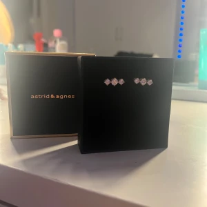 Guldörhängen med kristaller Astrid & Agnes - Snygga örhängen från Astrid & Agnes i guldton med tre glittrande vita kristaller på varje örhänge. Designen är stilren och modern, perfekt för att ge din look lite extra bling. Kommer i original ask.