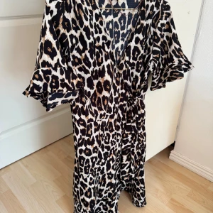 Leopardmönstrad klänning Pernilla Wahlgren - Snygg kortklänning från Pernilla Wahlgren med leopardmönster i svart, beige och brunt. Klänningen har v-ringning, knyt i midjan och korta ärmar med volang. Perfekt för dig som vill sticka ut med ett djurmönstrat plagg.