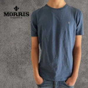 Blå t-shirt från Morris S - Snygg blå t-shirt från Morris med diskret guldfärgad logga på bröstet. Modellen är klassisk med rund hals och korta ärmar. T-shirten är gjord i mjuk bomull och har en clean, stilren look som funkar till jeans eller shorts.