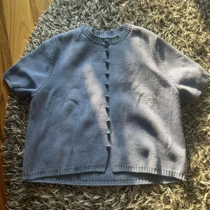 Blå kofta från Massimo Dutti - Kortärmad blå kofta från Massimo Dutti. Koftan har rund halsringning, ribbade kanter och knappar framtill i samma färg som plagget. Har några små fläckar men syns knappt.