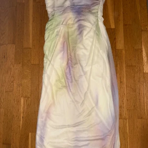 Pastellfärgad axelbandslös klänning Zara - Säljer en axelbandslös klänning från Zara i mjuka pastellfärger som lila, grön och rosa. Klänningen är helt ny och oanvänd,är figurnära med dragkedja i sidan och har en snygg omlott-effekt upptill. Materialet är polyester och längden är knälång.