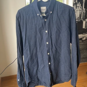 Mörkblå skjorta från Dobber - Snygg mörkblå skjorta från Dobber i storlek medium. Skjortan har klassisk krage, knäppning framtill med vita knappar och långa ärmar. Perfekt för dig som gillar en stilren och enkel look. Materialet känns mjukt och bekvämt mot huden.