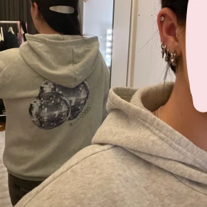 Grå hoodie med discokulor - Säljer en ljusgrå hoodie med tryck av två discokulor på ryggen. Lite nopprig💗