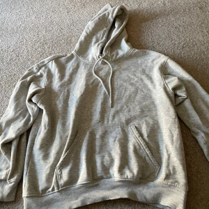 Grå hoodie från H&M loose fit - Säljer en ljusgrå hoodie från H&M i loose fit-modell. Tröjan har huva med snörning, magficka och ribbade muddar vid ärmslut och nederkant. Perfekt för chill dagar eller när du vill ha en enkel och clean look.