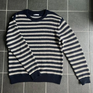 Randig stickad tröja från Zara - Säljer en stickad tröja från Zara i marinblått och vitt med horisontella ränder. Tröjan har rund hals, långa ärmar och ribbade muddar. Perfekt för dig som gillar en klassisk men ändå chill stil. Knappt använd, som ny! 