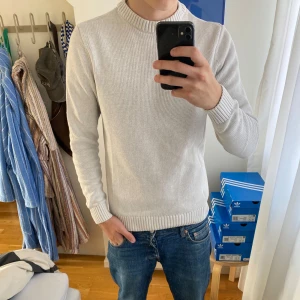 Ljusgrå stickad tröja från Dobber - Säljer en stilren ljusgrå stickad tröja från Dobber i storlek S. Tröjan har rund halsringning, ribbade muddar och är långärmad. Perfekt för lager-på-lager och enkel att matcha med jeans eller chinos.