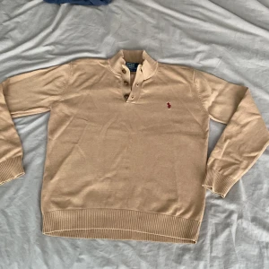 Beige stickad tröja Polo Ralph Lauren - Säljer en beige stickad tröja från Polo Ralph Lauren i storlek XS . (Barnstorlek Storlek L) Tröjan har ribbad krage, tre bruna knappar vid halsen. Lite trasig i ena armhålan men går enklet att sy ihop. Knapparna är lite lösa.