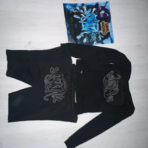 Black Syna World TrackSuit - Selling a Syna World tracksuit in black. The set includes a hoodie + sweatpants with the iconic Syna World print on the front and the hood.  ✅ Size: M (medium) ✅ Condition: Good – used and bought from a previous owner, some small loose threads (nothing that affects wear). ✅ Trendy streetwear / unisex fit.  Perfect for anyone who likes Syna World by Central Cee, streetwear, hip hop, and exclusive tracksuits.