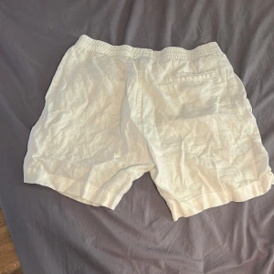Vita linneshorts från H&M - Säljer ett par vita shorts från H&M i regular fit. De är gjorda i svalt linne, har resår i midjan och fickor på sidorna samt en bakficka. Perfekta för varma dagar och enkel att matcha med allt. Pris går att diskuteras.