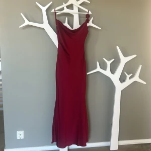 Vinröd balklänning med blomdetalj i ryggen - Säljer en vinröd långklänning med tunna axelband och öppen rygg. Klänningen har dekorativa blommor längs banden på ryggen och ett snyggt draperat fall. Perfekt för bal eller festliga tillfällen. Endast använd en gång på min bal!❤️ storlek 36. 