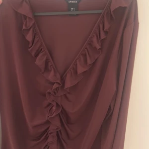 Vinröd omlottblus med volang Lindex - Supersnygg vinröd omlottblus från Lindex med långa ärmar och volangdetaljer längs v-ringningen. Blusen har en figurnära passform och är gjord i ett mjukt, lätt material som känns skönt mot huden. Perfekt för dig som gillar en chic och trendig look.