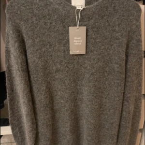 Grå ulltröja i alpackablandning H&M - Helt ny med pris lapp! Slutsåld Mysig grå tröja från H&M i en blandning av ull och alpacka. Tröjan har en klassisk rak passform och långa ärmar, perfekt för kyliga dagar. Den är supermjuk och fluffig, vilket gör den extra skön att ha på sig.