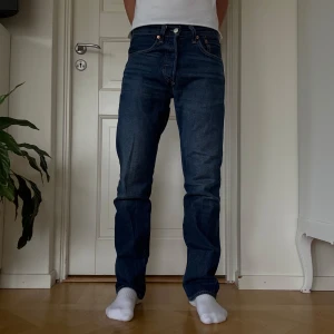 Levi's 501 mörkblå jeans 28/32 - Säljer ett par klassiska Levi's 501 jeans i mörkblå tvätt. Modellen har rak passform, normal midja och fem fickor. Jeansen är tillverkade i slitstarkt bomullsmaterial och har den ikoniska läderpatchen bak. Dom har i princip inga tecken på användning, ser nästan helt nya ut. Skriv om du vill ha mått eller fler bilder så fixar jag det!