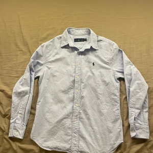 Ljusblå skjorta från Ralph Lauren - Klassisk ljusblå skjorta från Ralph Lauren med broderad logga på bröstet. Använd 3 eller 4 gånger och den är helt ren och i ett mycket bra skick. Storlek XS, män. Skickar inom 1-3 dagar och pris kan diskuteras 