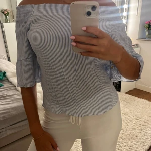 Randig offshoulder blus i blåvitt - Superfin blus med blå och vita ränder, offshoulder-modell och volangärmar i trekvartslängd. Perfekt för en fräsch och somrig look. Luftigt material som känns skönt mot huden.