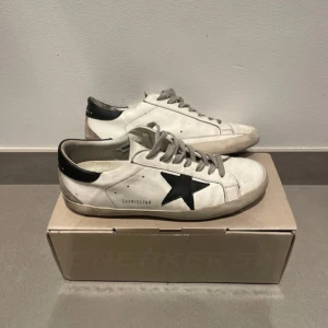 Golden Goose superstar svart stjärna - (Skorna är ej tvättade på bilderna) Ett par schyssta golden goose superstar i använt skick (därav priset) skorna är i bra skick förutom där back vid hälen där dem har börjat vissa tecken på att släpa (bild3). Problemet bör enkelt gå att fixa hos skomakare. Beställdes på Miinto förra sommaren. Bara att skriva vid frågor och priset är ej hugget. Storlek: 43 Nypris: ca 5000 Allt og medkommer