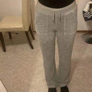 Grå juicy byxor - Mysiga grå mjukisbyxor med bred resår i midjan och snörning framtill. Byxorna har stora fickor fram och en ficka bak med knapp. Raka ben och mjukt material som känns skönt mot huden. Perfekta för chill dagar hemma.