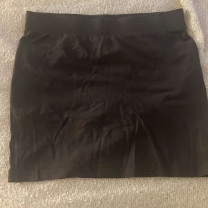 Svart kortkjol från H&M Divided - Enkel svart kortkjol från H&M Divided med bred resår i midjan. Kjolen är rak i modellen och tillverkad i mjuk bomullsblandning med lite stretch för en bekväm passform. Perfekt att styla med en oversized hoodie eller crop top.