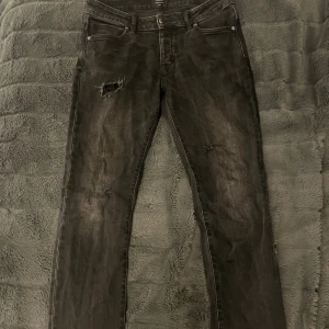 Svarta  jeans med slitningar från Neuw  - Säljer ett par svarta neuw jeans med snygga slitningar på låret och bakfickan. Jeansen har klassisk femficksdesign och en tight passform som sitter snyggt längs benen. 